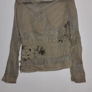 Unik tunn topp, st S, bli ensam om - Unik militär färg topp med broderade detaljer i grönt och svart. Toppen har långa ärmar och en intressant omlottdesign. Perfekt för dig som vill ha något annorlunda i garderoben.