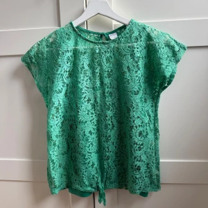 Grön spetsblus från Lindex - Säljer en söt grön spetsblus från Lindex med korta ärmar och knytning i ryggen. Perfekt för sommarens varma dagar. Matchande grönt linne ingår!! Passar både till vardag och festliga tillfällen :) säljer pga den är för liten. 