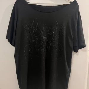 Svart t-shirt med rhinestones - Snygg svart t-shirt med ett subtilt glittrigt mönster på framsidan. T-shirten har korta ärmar och en bekväm passform. Obs: köpte på shein dock flera år sen. Några rhinestones e av