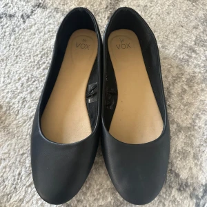 Svarta ballerinaskor från Vox - Snygga och stilrena svarta ballerinaskor från Vox. Perfekta för en enkel och bekväm look. De har en rund tå och är gjorda i ett mjukt material för extra komfort.