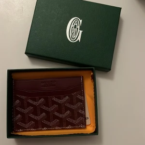 Mörkröd korthållare! - Säljer en unik mörkröd korthållare med ett ikoniskt mönster. Plånboken har flera fack för kort och är perfekt för den stilmedvetna. Kommer i originalförpackning, den e helt oanvänd! Fick den i present men har redan en! Priset kan diskuteras vid snabb affär! Box ingår ej