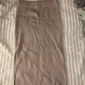 Beige ribbad kjol - Säljer en stilren beige ribbad kjol i lång modell från Gina i sorlet M passar även L. Perfekt för en elegant och avslappnad look. Kjolen har en mjuk och bekväm passform.