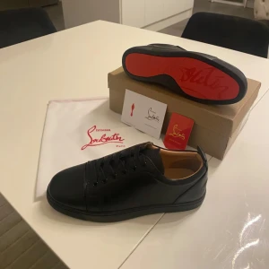 Louboutin skor - Snygga svarta sneakers från Christian Louboutin med den ikoniska röda sulan. Skorna har en stilren design med snörning och är tillverkade i skinn. Perfekta för den som vill ha en touch av lyx i vardagen. Helt ny.
