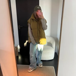 Olivgrön dunväst - Snygg olivgrön dunväst med dragkedja och hög krage. Perfekt för lager-på-lager under kyliga dagar. Västen har en avslappnad passform och är lätt att matcha med olika outfits. Använd 1 gång!