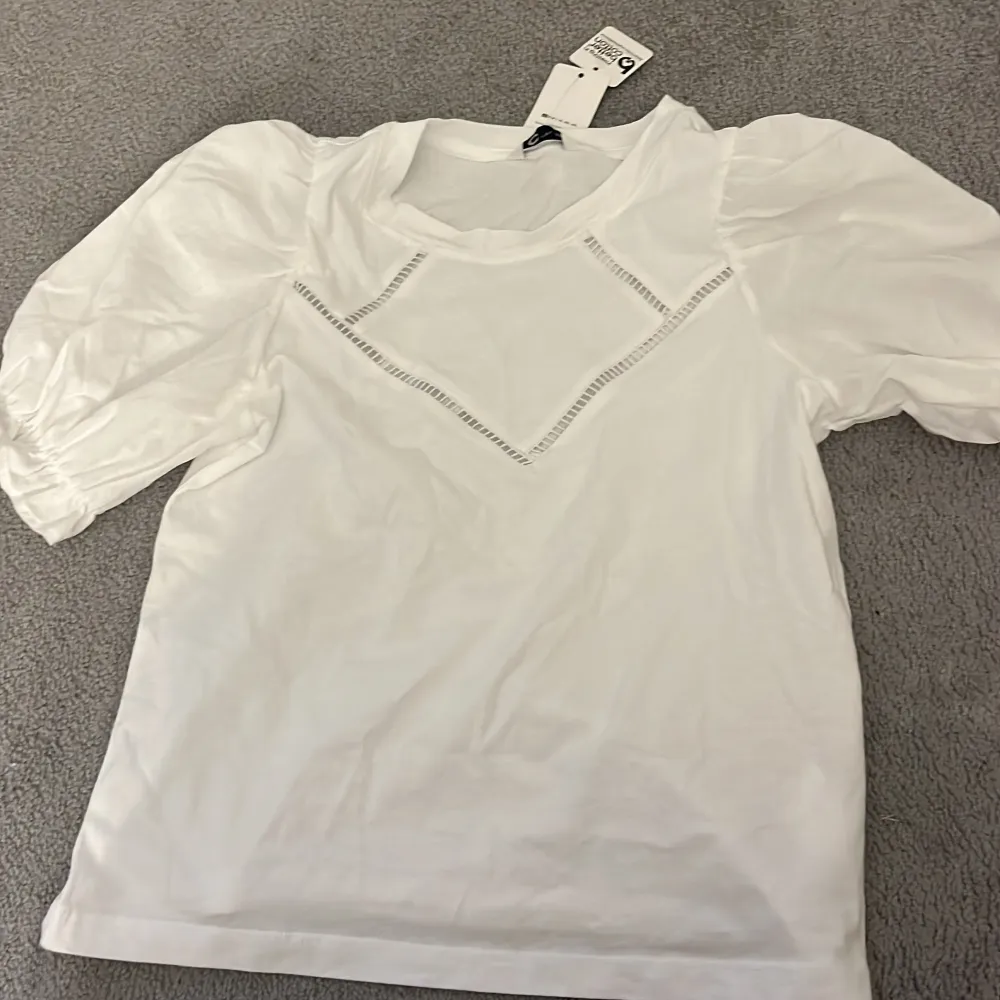 Säljer en stilren vit blus från Cubus med puffiga korta ärmar och dekorativa spetsdetaljer framtill. Perfekt för en elegant look. Blusen är i ett mjukt och bekvämt material. Aldrig använt . Yläosat.