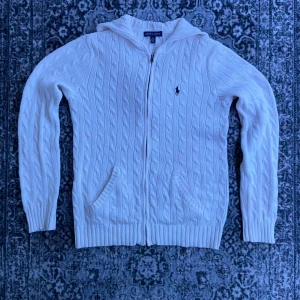 Vit stickad kofta från Ralph Lauren - Väldigt snygg lätt cableknit helzip hoodie Ralph lauren. Storlek M i helt fantastiskt skick! Tröjan är vit och marinblå. Nypris 3600kr.                                                                        Hör av dig vid frågor eller prisförslag!