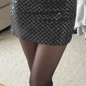 Paljett kjol - Snygg svart kortkjol med ett glittrigt mönster. Perfekt för att lysa upp kvällen med sitt eleganta och festliga utseende. Kjolen har en tight passform och är idealisk för speciella tillfällen. Storlek 32. Helt ny🪩🪩