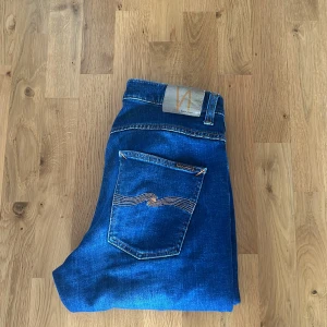 Blå jeans från Nudie Jeans - Snygga blå jeans från Nudie Jeans i modellen Grim . Klassisk design med fem fickor och orange sömmar. Perfekta för en avslappnad stil. Använda i en månad så i princip helt nya. Nypriset ligger på 1600.