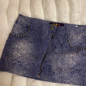 Mini-skirt från Exclusive Jean-Line - Snygg blå/lila kjol från Exclusive Jean-Line med unikt mönster och dragkedja fram. Kjolen har nitar vid fickorna som ger en cool detalj. Perfekt för att sticka ut i mängden!💓