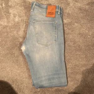 Ljusblå jeans från Replay - Snygga ljusblå jeans från Replay med en klassisk femficksdesign. De har en modern tvättad look och är tillverkade i ett bekvämt denimtyg. Perfekta för en avslappnad stil. Liten slitning i grenen men märks inte av! Skulle mer säga att de är som ett par 33 då dom är lite större i midjan 