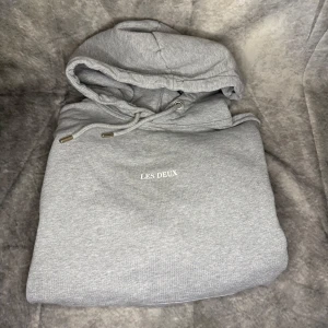 Grå hoodie från Les Deux - Säljer en stilren grå hoodie från Les Deux. Den har en klassisk design med en ficka framtill och luva med snören.  Skriv för fler frågor!