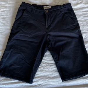 Mörkblå shorts från Hampton Republic - Snygga mörkblå shorts från Hampton Republic med knapp och dragkedja framtill. De har två sidofickor och två bakfickor med knappar. Perfekta för en avslappnad stil. Storlek 170. Anledningen till att de är lite skrynkliga är att de inte används på länge utan legat i garderoben då dom är för små för mig.