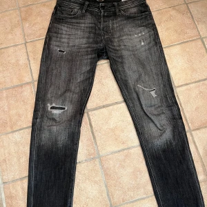 Svarta jeans med slitningar  - Snygga svarta jeans med slitningar. Tapered fit med storlek W32 L34. Inga tydliga tecken på användning. Priset ligger på 350kr