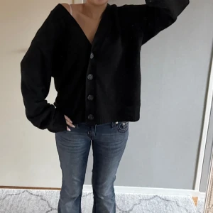 Svart kofta med knappar - Säljer en svart kofta med knappar framtill. Den har en v-ringad design och långa ärmar. Från nelly