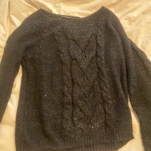 Svart stickad tröja - Säljer en svart stickad tröja med ett snyggt flätmönster framtill. Den har en subtil glittrig effekt som ger en extra touch. Perfekt för både vardag och speciella tillfällen. Snygg till en jeans kjol på sommaren. 