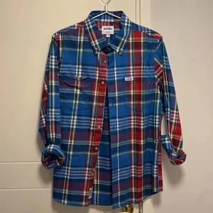 Rutig skjorta från Etnies - Säljer en färgglad rutig skjorta från Etnies i storlek S. Skjortan har en mix av blå, röd och grön färg med knappar framtill och två bröstfickor. Perfekt för en avslappnad stil.