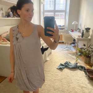 Ljuslila klänning från H&M - Säljer en söt ljuslila klänning från H&M med en unik blomdetalj på axeln. Klänningen är ärmlös och har en avslappnad passform som gör den perfekt för varma dagar. Den är tillverkad i ett mjukt och bekvämt material.