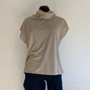 Beige polotopp - Snygg beige polotopp med korta ärmar och en lös passform. Perfekt för en stilren look, oavsett tillfälle. Den mjuka färgen gör den lätt att matcha med olika outfits.