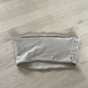 Grå ribbad tubtopp - Säljer en stilren grå ribbad tubtopp. Perfekt för en minimalistisk look och lätt att matcha med olika outfits. Toppen är elastisk och bekväm att bära.