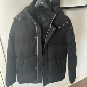 Svart dunjacka från Moose Knuckles - Säljer en snygg svart dunjacka från Moose Knuckles i storlek S. Jackan har en dragkedja framtill och flera fickor med tryckknappar. Den är perfekt för kalla dagar och har en stilren design med märkets logga på ärmen. Ordpris var 10 000kr. Säljs istället för 6800kr. Pris går att diskuteras!!
