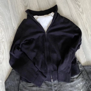 Svart merinoulltröja från These Glory Days - Säljer en stilren svart tröja i merinoull från These Glory Days. Tröjan har en dragkedja framtill och långa ärmar, perfekt för kyligare dagar. Den är mjuk och bekväm med ribbade muddar vid ärmslut och nederkant.