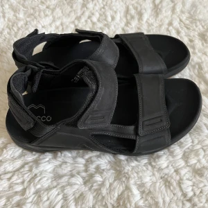 Helt nya Svarta sandaler från Ecco - Helt nya, oanvända sandaler. Snygga och bekväma svarta sandaler från Ecco med justerbara remmar för perfekt passform. Sandalerna har en slitstark sula och är perfekta för sommarens äventyr. STORLEK 41. Pris kan diskuteras