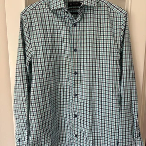 Rutig kostymskjorta från Riley - Snygg rutig kostymskjorta från Riley i blått, grönt och vitt. Skjortan har en klassisk krage med breda slag och färgade knappar framtill. Använd fåtal gånger. 