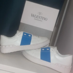 Valentino Garavani  - Snygga Valentino Garavani sneakers i vitt skinn med en iögonfallande blå detalj på sidan. Skorna har en klassisk rund tå och en stilren design som passar perfekt för en trendig look. Använda 1 dag säljer eftersom den e för små 