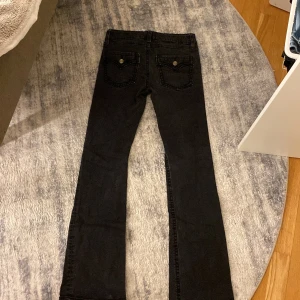 Svarta bootcut jeans från Gina tricot Young  - Snygga svarta bootcut jeans från Gina young med klassisk femficksdesign och dragkedja. Jeansen har en knappdetalj på bakfickorna och är perfekta för en stilren look.