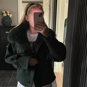 Mörkgrön jacka med pälsdetalj från Meotine - Säljer en mörkgrön jacka från Meotine med en lyxig pälsdetalj vid kragen. Jackan har en croppad passform och knappar framtill. Perfekt för att hålla stilen i kyligare väder. Är i otroligt bra skick! Kan gå ner i pris vid snabb affär 
