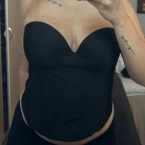 Svart axelbandslös korsett - Snygg svart axelbandslös korsett med en elegant och stilren design. Perfekt för att skapa en chic look. Den har en slät yta och en bekväm passform som framhäver figuren.