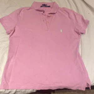 Rosa pikétröja från Polo - Säljer en stilren rosa pikétröja från Polo i storlek L. Tröjan har en klassisk krage och korta ärmar, perfekt för en avslappnad look. Den är slim fit och har en liten broderad logga på bröstet.OBS! Och ett oerhört litet hål på höger sida. Den är liten i strl(passar it mig som har L/XL)