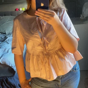 Rosa blus med knytning - Säljer en söt rosa blus med knytning framtill. Blusen har korta ärmar och en lös passform som ger en avslappnad look. Perfekt för vår och sommar!