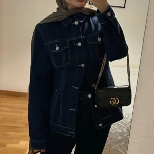 Mörkblå jeansjacka - Snygg mörkblå jeansjacka med knappar framtill och två bröstfickor. Jackan har en klassisk krage och långa ärmar. Perfekt för en stilren look.