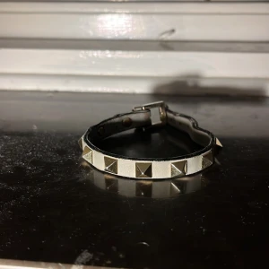 Vitt bälte med nitar från valentino - Snyggt vitt bälte med silverfärgade nitar som ger en edgy look. Perfekt för att ge din outfit lite extra attityd. Bältet har ett klassiskt spänne och är tillverkat i ett material som liknar skinn.