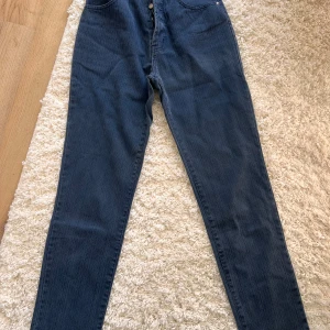 Blå jeansbyxor från Cha Cha  - Snygga blå jeansbyxor från Cha Cha med knappgylf och klassisk femficksdesign. Byxorna har en rak passform och är perfekta för en avslappnad stil. Märkeslappen baktill ger en extra touch. 