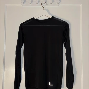 Svart långärmad tröja från Ronhill - Säljer en svart långärmad tröja från Ronhill. Perfekt för träning med sitt lätta och bekväma material. Tröjan har en enkel design med rund hals och är tillverkad i syntetmaterial för optimal andningsförmåga.