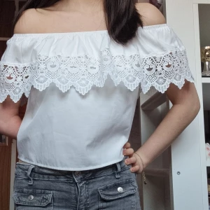 Vit offshoulder topp med spetsdetaljer - Säljer en söt vit offshoulder topp med vackra spetsdetaljer runt axlarna. Perfekt för sommarens varma dagar. Toppen har en luftig passform och är tillverkad i ett lätt material.