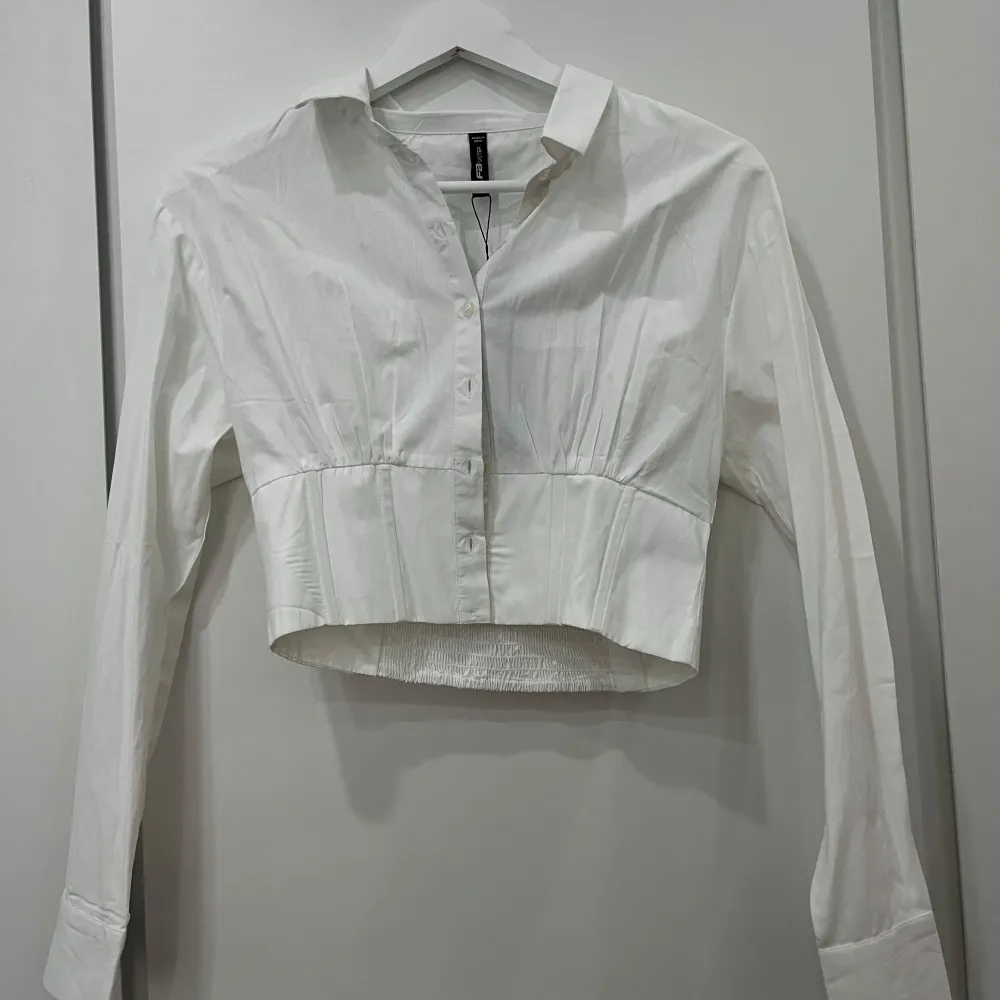 Säljer en stilren vit croppad blus från newyorker med knappar framtill. Blusen har långa ärmar och en smickrande passform med elastisk detalj i ryggen. Perfekt för en chic look! Korsett skjorta! Helt ny! Nypris 170. . Paidat.