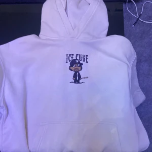 Vit hoodie med Ice Cube-tryck från H&M - Vit hoodie från H&M med ett tryck av Ice Cube på bröstet. Tröjan har en oversized passform, huva och magficka. Perfekt för dig som gillar streetwear och vill ha en bekväm och stilren look. Storlek S