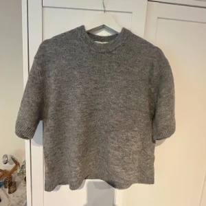 Grå stickad tröja från Gina Tricot - Mysig grå stickad tröja från Gina Tricot i ullblandning. Tröjan har korta ärmar, rund halsringning och en något boxig passform. Perfekt för lager-på-lager och enkel att matcha med olika outfits. Helt ny . Ord pris 300