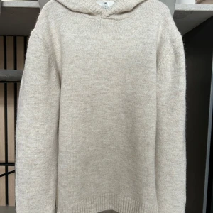 Beige stickad hoodie från H&M - Mysig beige stickad hoodie från H&M med normal passform. Tröjan har långa ärmar, huva och ribbade muddar vid ärmslut och nederkant. Perfekt för kyliga dagar och enkel att matcha med jeans eller andra byxor.