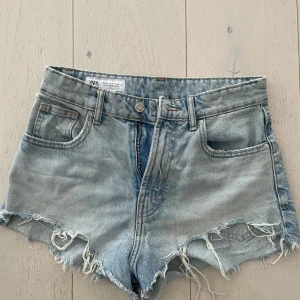 Ljusblå jeansshorts med fransar från Zara - Säljer ett par ljusblå jeansshorts från Zara i bra skick som tyvärr blivit för små för mig. Shortsen har medelhög midja, med fransade kanter och klassisk femficksdesign.
