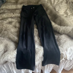Svarta velourbyxor från Juicy Couture - Säljer ett par svarta velourbyxor från Juicy Couture med broderad JC-logga på fickan. Byxorna har normal passform och vida ben, samt resår i midjan med dragsko. Perfekta för en avslappnad och trendig look.🪩