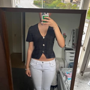 Svart blus med knappar från Gina Tricot - Säljer en svart blus från Gina Tricot i storlek XS. Blusen har korta ärmar, v-ringning och dekorativa knappar framtill. Modellen är figurnära och passar perfekt till både jeans och kjol. Använd fåtal gånger!