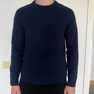 Mörkblå stickad tröja från A day’s march  - En enkel och stilren mörkblå stickad tröja med rund halsringning och långa ärmar. Tröjan har en klassisk passform och ribbade muddar vid ärmslut och nederkant..