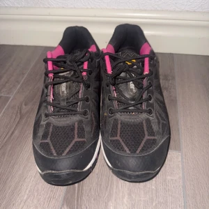 Svarta och rosa sneakers från Monitor - Säljer ett par svarta sneakers från Monitor med rosa detaljer och svarta skosnören. Skorna har en vit och rosa sula med mönstrad undersida och är tillverkade i syntetmaterial. Perfekta för dig som gillar sportig stil.
