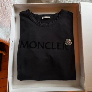 Svart t-shirt från Moncler - Mörkblå t-shirt från Moncler med ”Moncler” text och loggan på bröstet. Perfekt för en stilren och avslappnad look och perfekt för sommaren.               Skick 8/10 boxen ingår, tyvärr inget kvitto             100% äkta | Nypris runt 3000 kr | För fler bilder är det bara och fråga. 