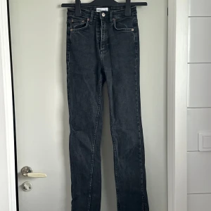 Svarta bootcut jeans från Zara - Säljer ett par svarta bootcut jeans från Zara i storlek XS. Jeansen har hög midja, klassisk femficksdesign och en liten slits nertill på benen. Perfekta för dig som gillar en tidlös och stilren look. Jag vet att de verkar vara hemsk långa på bilden, men det är dem i verkligheten inte. 
