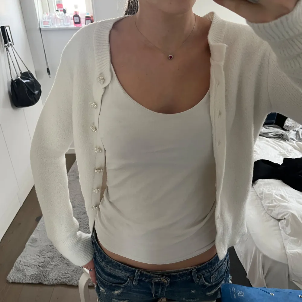 Säljer en söt vit kofta med unika pärlknappar. Koftan är stickad och har lång ärm, perfekt för lager-på-lager. Enkel att matcha till olika outfits och ger en stilren look.. Neuletakit & Villapaidat.